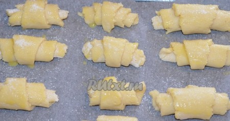 Выложить рогалики на противень, застеленный пергаментом, смазать поверхность молоком и посыпать сахаром (благодаря сахару, корочка будет более хрустящей). Выпекать печенье из творога в разогретой духовке при температуре 200 градусов минут 20-30 (до золотистого цвета).