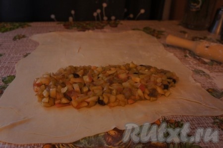 Слоёное тесто заранее достаём из морозилки и оставляем размораживаться. Размороженное слоёное бездрожжевое тесто делим на 2 части. На столе, припылённом мукой, одну часть теста раскатываем в довольно тонкий прямоугольный пласт, выкладываем яблочную начинку ближе к одному из краёв, оставляя края теста чистыми. Подворачиваем длинные края теста, слегка накрывая начинку, а затем сворачиваем тесто с начинкой в рулет, начиная со стороны с начинкой.