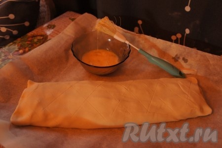 Слегка надавливая ножом, делаем на поверхности слоёного теста надрезы. Перекладываем штрудель с яблоками на противень, застеленный пергаментной бумагой. Смазываем штрудель взбитым яйцом.