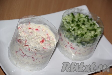 Крабовые палочки мелко нарезать, выложить поверх риса, смазать плавленным сыром, немного утрамбовать. Огурец вымыть, обсушить, нарезать на мелкие кубики, выложить поверх сыра, слегка утрамбовывать.