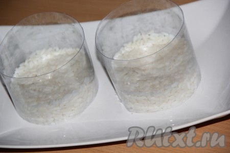 Я делала порционную подачу салата, для этого использовала 2 пластиковых бортика, но можно формировать и с помощью сервировочных колец. Также можно сформировать салат и в одном большом салатнике. Поскольку я делала 2 порции салата, поэтому и все составляющие салата равномерно раскладывала по 2 формам. На плоскую тарелку поставить бортики, на дно выложить рис, смазать майонезом, слегка утрамбовать.