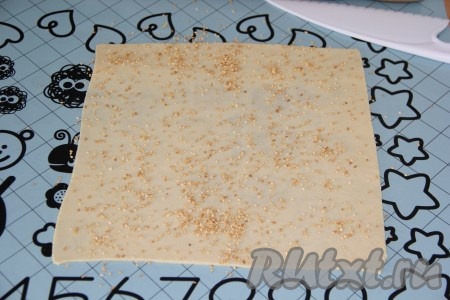 На присыпанной мукой поверхности вначале первую часть теста раскатать в достаточно тонкий прямоугольник. Можно воспользоваться ножом и выровнять края прямоугольника. Первый пласт теста посыпать кунжутом.&nbsp;