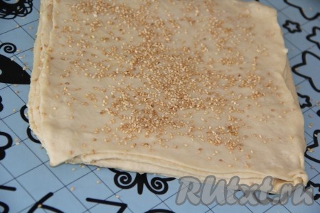 Раскатать вторую часть теста в пласт, выровнять края пласта так, чтобы получился прямоугольник такого же размера, как и прямоугольник из первой части теста. Второй пласт выложить поверх первого, присыпать кунжутом. Таким образом постепенно раскатать все части теста, выкладывать их друг на друга, не забывая посыпать кунжутом. У меня из обрезков получился ещё один пласт теста. Итого у нас получилась слоёная заготовка из 7 пластов теста.