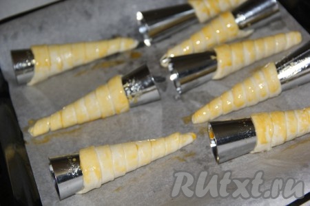 Противень для выпекания застелить пергаментной бумагой. Выложить трубочки на пергамент, отступая немного места друг от друга, так как при выпекании слоеные трубочки увеличатся в размере. Смазать трубочки взбитым яичным желтком. Поставить противень в разогретую духовку.
