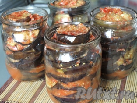 Банки простерилизовать удобным для вас способом. На дно выложить пару ложек перечно-чесночной массы. Наполнять банки баклажанами, немного прослаивая их перечно-чесночной смесью. В глубокую кастрюлю на дно положить тканевую салфетку, поставить наполненные баклажанами банки, залить горячей водой по плечики и стерилизовать с момента закипания воды 8-10 минут.