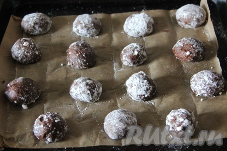 По истечении времени достаём тесто для будущего шоколадного печенья и формируем 35 шариков. Каждый шарик тщательно обваливаем в сахарной пудре. Выкладываем шарики на противень, застеленный пергаментной бумагой, на достаточно большом расстоянии друг от друга.