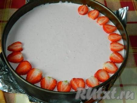 Дно разъёмной формы, в которой выпекался бисквит, застелить фольгой, выложить полностью остывший бисквит, зажать его в форму (то есть просто закрыть бортики формы). Выложить творожный крем на бисквит, разровнять и убрать в холодильник для застывания на несколько часов. Застывший клубничный торт из формы не вынимаем, а сразу украшаем клубникой, нарезанной на пластины.