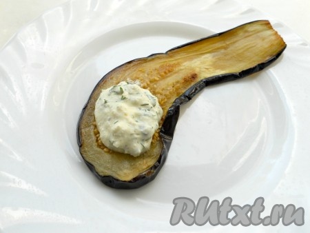 На широкую сторону остывшей пластины баклажана, немного отступив от краёв, поместить 1 чайную ложку начинки из творога и чеснока. Начиная со стороны с начинкой, свернуть баклажан в рулетик.&nbsp;
