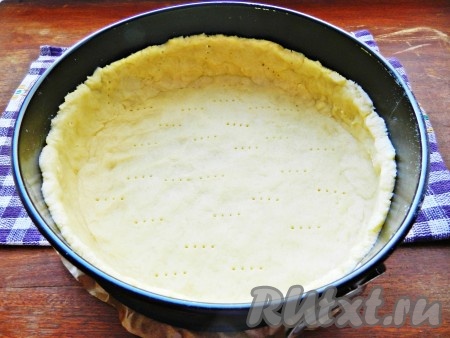 Форму для выпечки диаметром 21-23 сантиметра застелить пергаментной бумагой, немного смазать маслом. Тесто распределить по форме, сформировав бортики. Наколоть тесто вилкой. Форму с тестом накрыть плёнкой и убрать в холодильник на 30 минут.