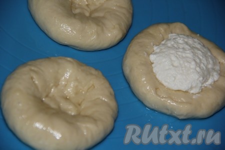Подошедшее тесто выкладываем на поверхность, смазанную растительным маслом, и хорошо обминаем. Делим тесто на небольшие части (на 14-16 штук), формируя из каждой части лепёшку с углублением. В середину каждой лепёшки выкладываем часть творожной начинки.