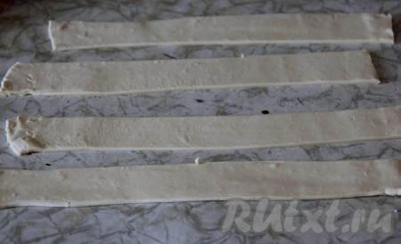 Слоёное тесто заранее разморозить при комнатной температуре. На присыпанной мукой поверхности раскатать слоёное тесто в пласт толщиной 2 миллиметра, а затем нарезать на полоски шириной 2 сантиметра (у меня длина полосок теста получилась 15 сантиметров).