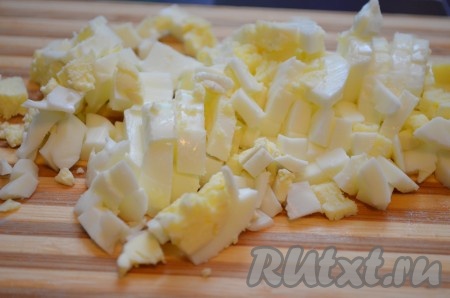 Отварить 2 яйца в течение 10 минут после закипания воды, а затем остудить их, очистить, нарезать на небольшие кубики.