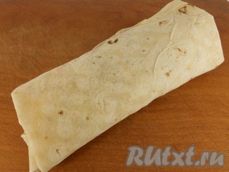 Подвернуть вначале боковые (более длинные) стороны лаваша на начинку, а затем, начиная со стороны с начинкой, свернуть лаваш в рулетик.