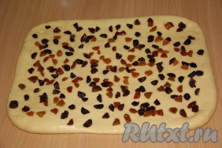 Поднявшееся тесто хорошо обминаем. На присыпанной мукой поверхности раскатываем тесто в прямоугольный пласт, смазываем растительным маслом и выкладываем изюм.