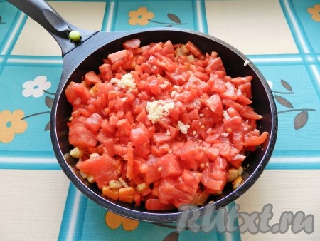 С помидоров снять кожицу, нарезать кубиками, выложить к остальным овощам. Чеснок пропустить через пресс. Все перемешать, уменьшить огонь и потомить под крышкой 6-8 минут.
