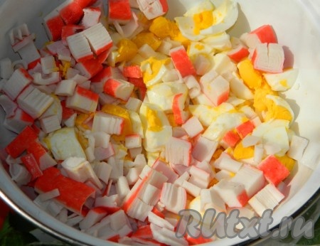 Яйца отварить в течение минут 8-10 с начала кипения воды, затем дать им полностью остыть и очистить. Крабовые палочки разморозить при комнатной температуре, освободить от плёнки. Крабовые палочки и варёные яйца нарезать не очень мелко и выложить в миску.
