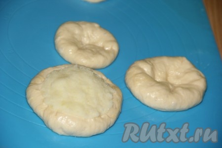 Тесто разделить на небольшие части. Из каждой части сформировать толстую лепёшку с углублением в середине. Выложить начинку в середину лепёшки.
