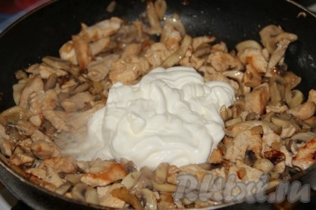 Затем в сковороду с шампиньонами и куриным филе выкладываем сметану, перемешиваем, вливаем 200 миллилитров тёплой воды, солим, перчим по вкусу, перемешиваем и после закипания соуса тушим на небольшом огне под крышкой 10 минут.