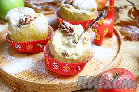 Яблоки выложить в форму для выпечки, влить немного воды и поставить в заранее разогретую до 200 градусов духовку, запекать 25-40 минут. Продолжительность запекания зависит от сорта яблок и их размера. Яблочки должны стать достаточно мягкими (легко прокалываться зубочисткой), но при этом хорошо держать форму. Яблоки, запечённые с сыром, освободить от фольги, переложить на тарелку (или в десертные ёмкости), чуть охладить, посыпать сахарной пудрой, украсить орешком и подать на стол.