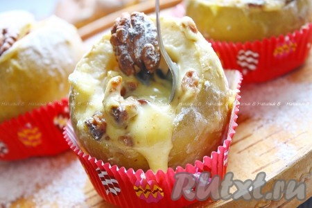 Яблоки выложить в форму для выпечки, влить немного воды и поставить в заранее разогретую до 200 градусов духовку, запекать 25-40 минут. Продолжительность запекания зависит от сорта яблок и их размера. Яблочки должны стать достаточно мягкими (легко прокалываться зубочисткой), но при этом хорошо держать форму. Яблоки, запечённые с сыром, освободить от фольги, переложить на тарелку (или в десертные ёмкости), чуть охладить, густо посыпать сахарной пудрой, украсить орешком и подать на стол.