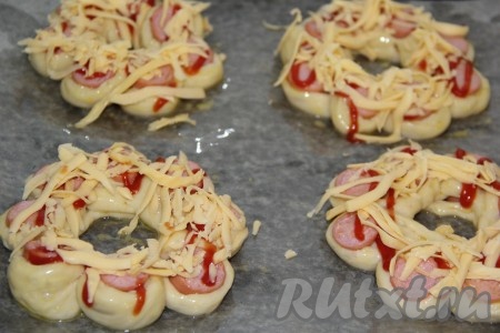 Сыр натереть на крупной тёрке и посыпать верх булочек. Поставить сосиски в тесте в разогретую духовку и выпекать "цветочки" при 180 градусах до золотистого цвета.
