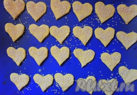 Духовку разогреть до 180 градусов. Противень застелить пекарской бумагой (или силиконовым ковриком), выложить заготовки сырных крекеров. Смазать печенье взбитым яйцом и обильно присыпать кунжутом.