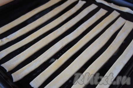 Противень смазать растительным маслом (или застелить пергаментом), выложить полоски из слоёного теста. В небольшую ёмкость разбить яйцо, взболтать вилкой до однородности. Смазать поверхность палочек из слоёного теста взбитым яйцом.