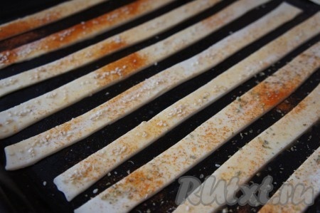 Посыпать палочки из слоёного теста кунжутом, немного посолить. По желанию, их можно присыпать специями (например, паприкой, чёрным молотым перцем, орегано). Поставить противень в духовку, разогретую до 180 градусов. Выпекать палочки до подрумянивания теста (примерно 20 минут).