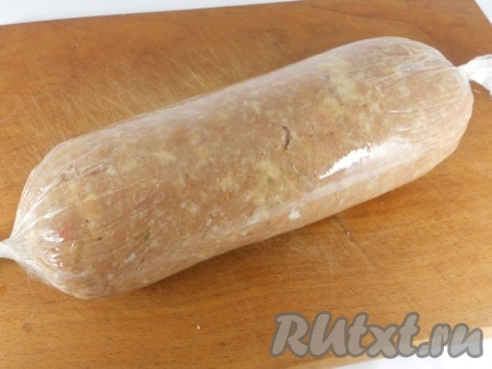 Далее с помощью плёнки, начиная с широкой стороны прямоугольника, свернуть фарш в рулет. Концы плёнки закрутить, чтобы получилась плотная колбаска.