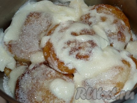 Поливаем сырнички сметаной, посыпаем сахаром, накрываем кастрюлю крышкой и тушим на маленьком огне минут 10.
