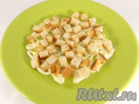 Ломти хлеба порезать маленькими кубиками. Обжарить их на сковороде с небольшим количеством (1 чайная ложка) растительного масла до легкой румяности. Остудить. Можно использовать и готовые сухарики в пакетиках, например, со вкусом красной икры. На дно круглой тарелки нанести сеточку из майонеза. Сухарики выложить на майонез первым слоем.
