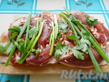 Зубчики чеснока очистить. Зелёный лук и петрушку промыть водой и обсушить. Присыпать мясо рубленным чесноком, выложить лук и петрушку.