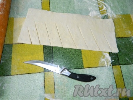 Слоёное тесто заранее достаём из морозилки и размораживаем. Два листа слоёного теста на присыпанной мукой поверхности раскатываем на одинаковые куски. Один лист теста выкладываем на противень, застеленный пергаментной бумагой. Второй лист слегка присыпаем 1 столовой ложкой муки, складываем пополам и делаем ножом косые разрезы со стороны сгиба, как на фото.