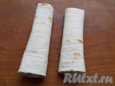 Подвернуть длинные края лаваша на начинку, а затем, начиная со стороны с сырной начинкой, свернуть лаваш в трубочку. Постепенно сформировать все трубочки. Оставить трубочки на 3-4 минуты, чтобы лаваш немного пропитался начинкой.