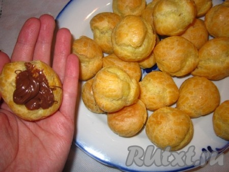 Достаем профитроли из духовки. Как только они остынут, можно их начинять. Набираем в кондитерский шприц начинку и, надломив серединку пирожного, наполняем профитроли нутеллой (если нет шприца, то можно воспользоваться чайной ложкой), верх тоже украшаем нутеллой.
