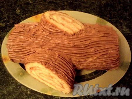 Формируем наше Рождественское полено. Обрезаем края рулета с двух сторон, чтобы был красивый разрез. Отрезаем&nbsp; от рулета кусочек толщиной 7-8 см и разрезаем его наискосок. С помощью крема приклеиваем кусочки к рулету - это будут сучки полена. Смазываем рулет шоколадно-ореховым кремом и вилкой наносим рисунок коры.
