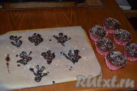 На пергаментной бумаге растопленным шоколадом, выложенным в пакет, нарисовать деревья. Присыпать кокосовой стружкой и кондитерской посыпкой. Убрать в морозильную камеру на 5-7 минут. Остатками шоколада смазать поверхность остывших кексов.
