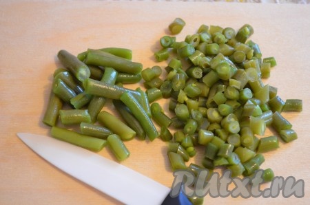 Стручки спаржевой фасоли промыть водой, отрезать "хвостики" с двух сторон, затем нарезать на части, выложить в кастрюлю с кипящей водой, ещё раз дать закипеть и отварить до мягкости (в течение 5-7 минут). Варёную фасоль откинуть на дуршлаг, обдать холодной водой, дать лишней воде стечь. Если фасоль покупная, то время варки смотрите на упаковке. Фасоль нарезать на маленькие кусочки, как на фото.