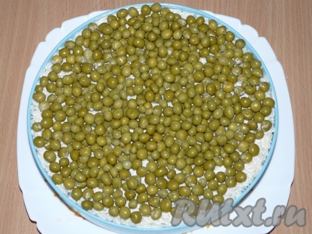 С горошка слить жидкость. Выложить слой горошка поверх салата. Покрыть всё пищевой плёнкой и убрать в холодильник на пару часов.
