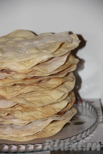 Полученное тесто разделить на 20 частей. Каждую часть раскатать в круг диаметром 24 см. Коржи получаются тонкими, как пергаментная бумага. С помощью тарелки такого же диаметра, как корж, обрезать края и наколоть корж вилкой. Запечь коржи в духовке примерно по 1-2 минуте при температуре 200 градусов, в зависимости от духовки. Выпекать на противне или на пергаментной чистой бумаге. Таким образом выпечь все 20 коржей.
