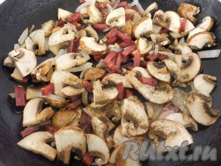 Шампиньоны промыть водой, нарезать на тонкие пластины, добавить к луку и колбасе. Посолить, посыпать специями по вкусу. Обжаривать всё вместе 3-4 минуты, иногда перемешивая.