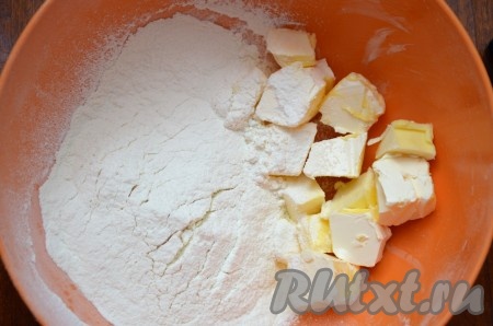 Сливочное масло достать из холодильника, нарезать на кусочки, выложить в объёмную миску, всыпать 200 грамм муки.
