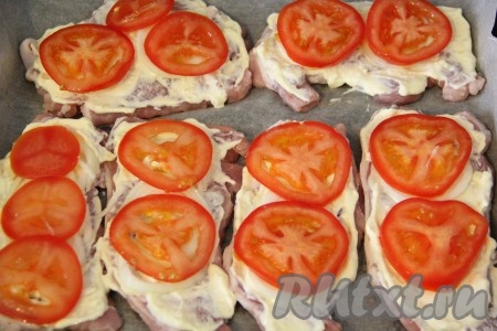 Помидоры вымыть и порезать на тонкие кружочки. Выложить кружочки помидоров поверх лука. Поставить противень со свининой в разогретую духовку и запекать при температуре 200 градусов 20 минут.
