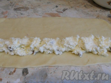 Каждую часть теста раскатать в небольшой пласт толщиной около 0,5 сантиметра. Мука для раскатки не нужна. Творожную начинку зрительно разделить на 6 частей (по количеству частей дрожжевого теста). Выложить в длину одну часть творожной начинки ближе к одному из краёв, как на фото.