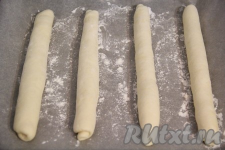 Противень застелить пергаментной бумагой и слегка присыпать мукой. Выложить заготовки домашних багетов на противень швом вниз, чтобы при выпекании они не развернулись.