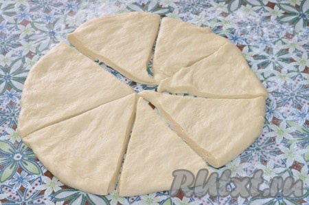 Поднявшееся тесто нужно немного обмять и, накрыв полотенцем, оставить в тёплом месте ещё на 20-30 минут. Затем выложить тесто на стол, поделить на 2 части. Каждую часть теста на присыпанном мукой столе размять в круг толщиной 1 сантиметр. Разрезать круг на 7-8 сегментов.