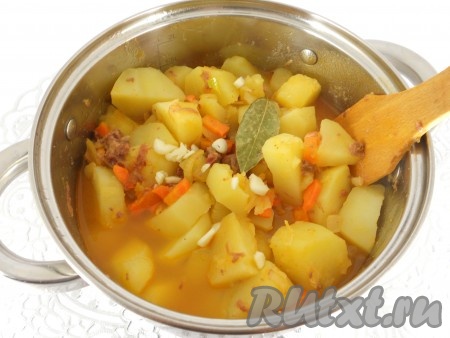 Когда картофель будет готов, высыпать в кастрюлю тушенку с овощами. Добавить порезанный чеснок и лавровый лист. Перемешать.