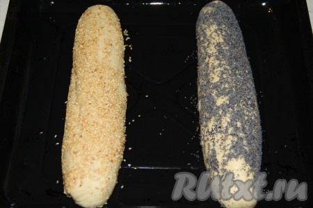 Сбрызнуть поверхность теста водичкой и посыпать наши будущие батоны кунжутом и маком. Посыпку можно выбирать по желанию, например, можно использовать семена тыквы, подсолнечника или льна. Противень для выпекания смазать растительным маслом или застелить пергаментом. Переложить батоны на подготовленный противень.