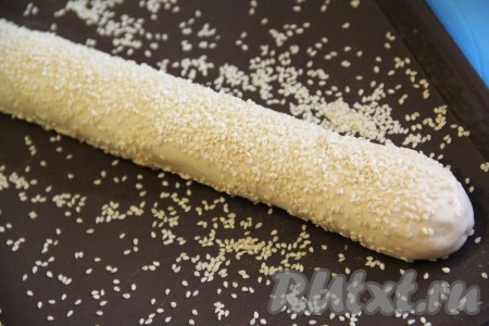 Смазать заготовки багетов водой (или молоком) и щедро посыпать кунжутом.