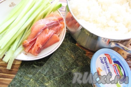 Количество продуктов берите по своей потребности, я всегда делаю большое количество роллов. Рис для приготовления суши тщательно промыть. Я высыпаю рис в сито и промываю под проточной водой. Выложить рис в кастрюлю и залить водой. Поставить кастрюлю с рисом на средний огонь. Довести рис до кипения, затем убавить огонь и варить рис под крышкой 15 минут. Готовый рис снять с огня, лишнюю воду слить, добавить рисовый уксус, хорошо перемешать. Накрыть кастрюлю с рисом полотенцем и остудить. Листы нори разрезать пополам. Рыбу нарезать на длинные кусочки. Огурец очистить от кожуры, нарезать длинными брусочками.
